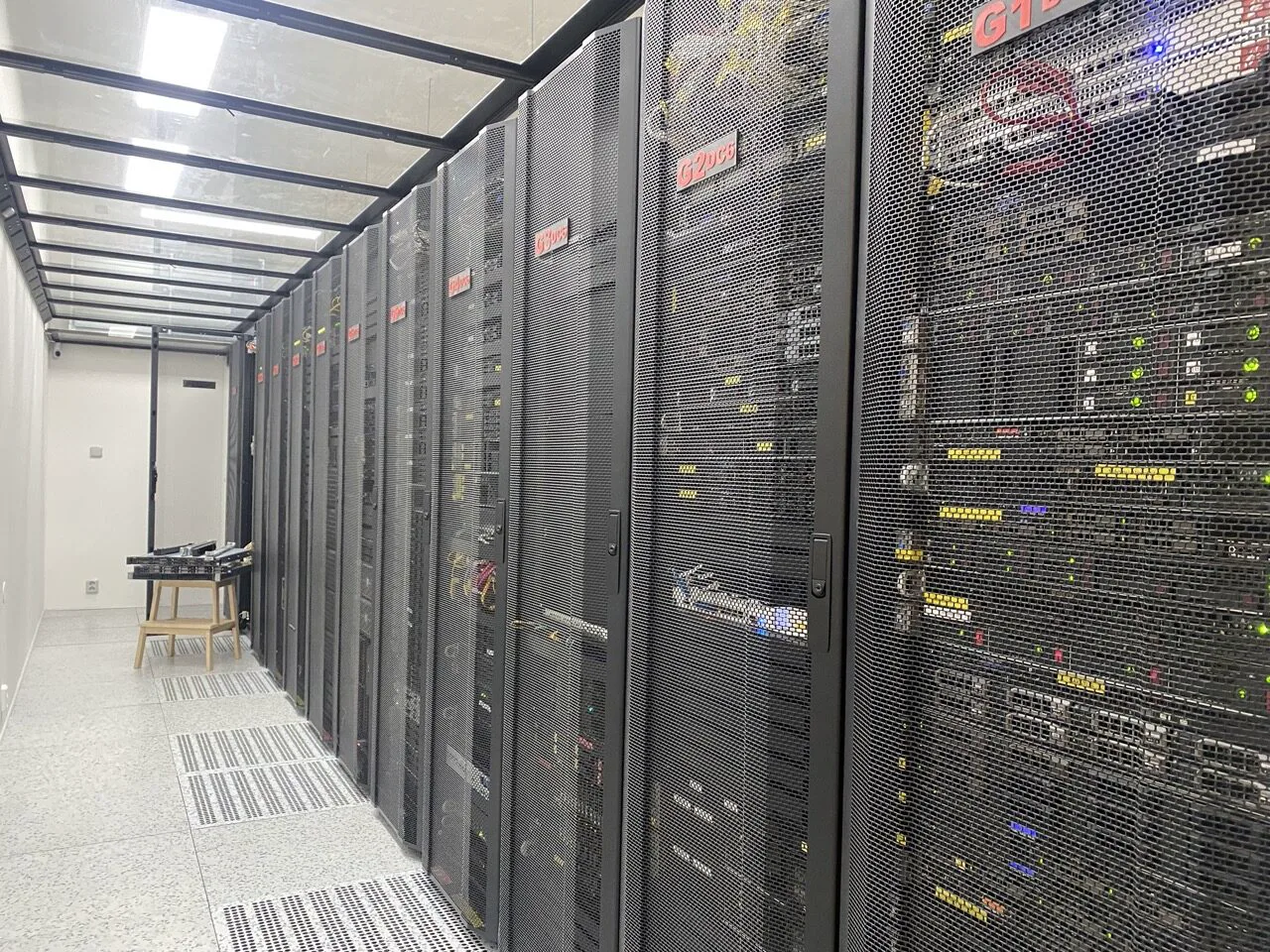 Ulička datacentra DC6 Vokovice: černé síťované racky s červenými štítky a běžícími servery.